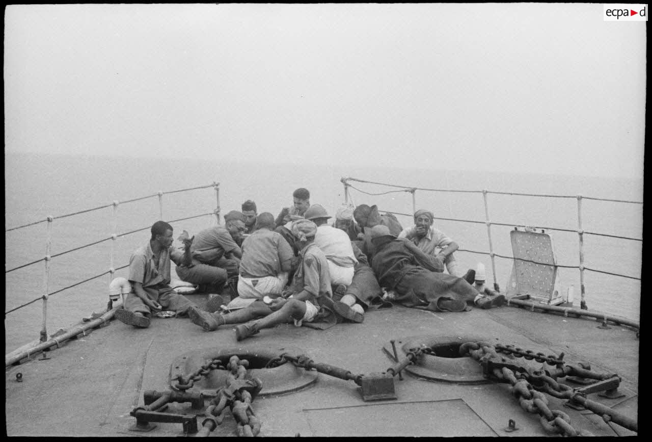 Des tirailleurs du 1er régiment de tirailleurs marocains (RTM) se restaurent sur le pont avant d'un torpilleur ou contre-torpilleur naviguant vers la Corse.