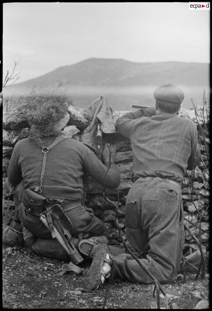 Un tirailleur marocain et un résistant corse sont postés derrière un mur de pierres dans le maquis, dans le secteur du col de San Stefano.