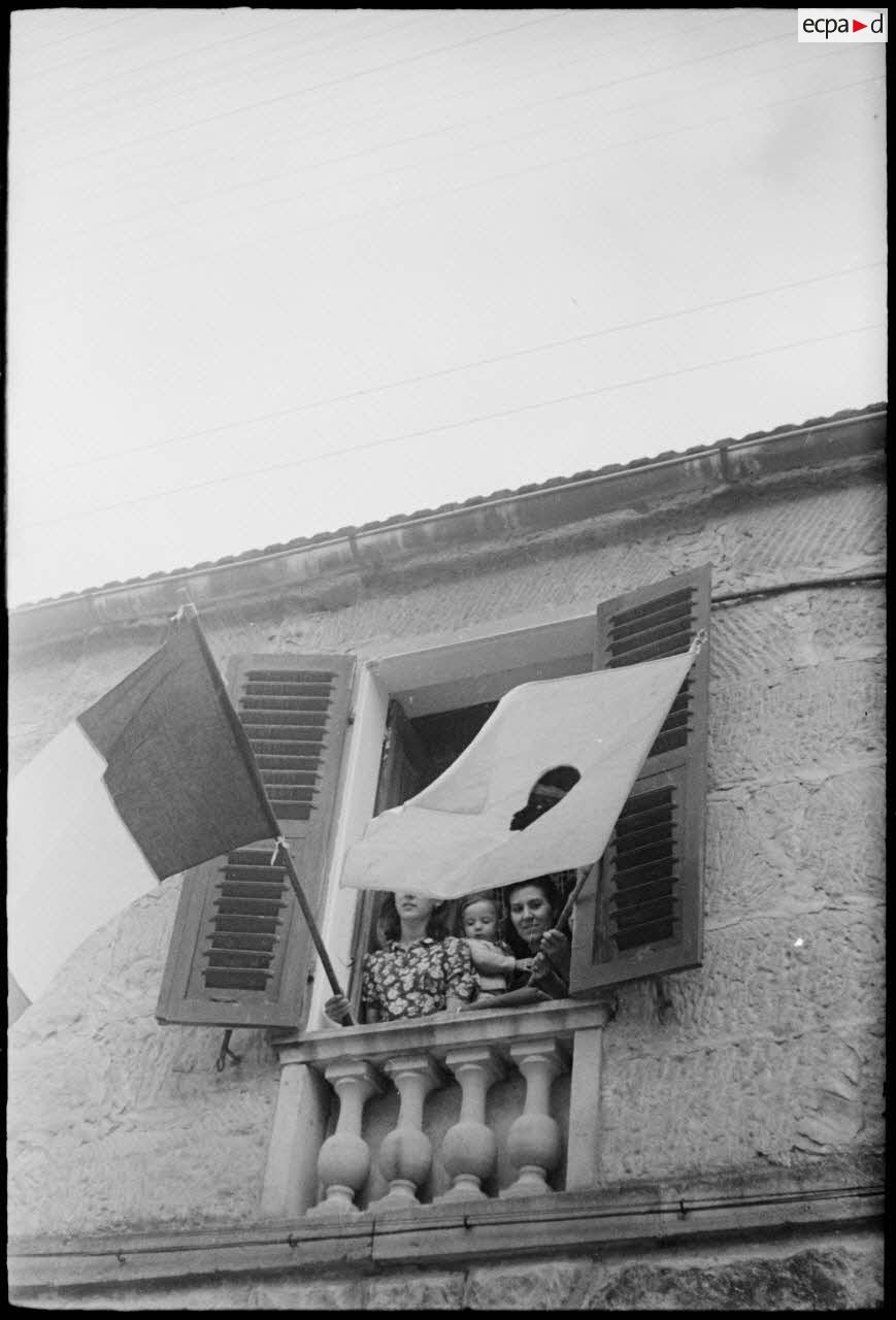 Des femmes pavoisent, avec les drapeaux français et corse, la fenêtre d'une maison de la commune de Saint-Florent qui vient d'être libérée.