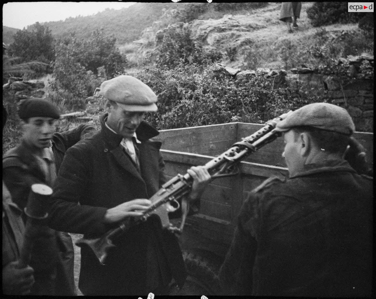 Des partisans corses examinent du matériel abandonné par les Allemands et entreposé dans un camion : des casques, une MG-34 et son chargeur circulaire.