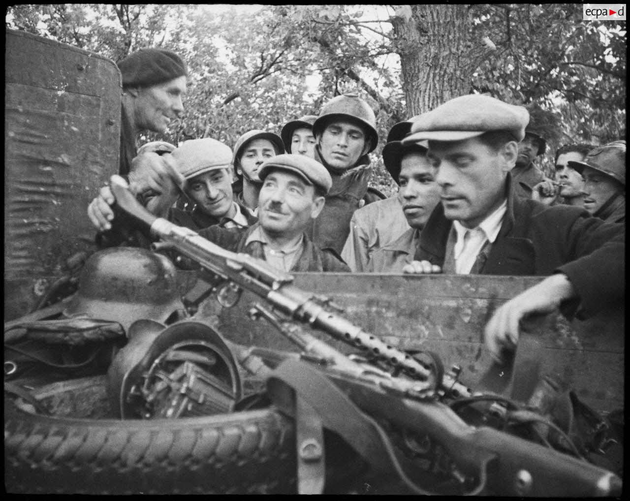 Des partisans corses examinent du matériel abandonné par les Allemands et entreposé dans un camion : des casques, une mitrailleuse MG-34 et son chargeur circulaire.