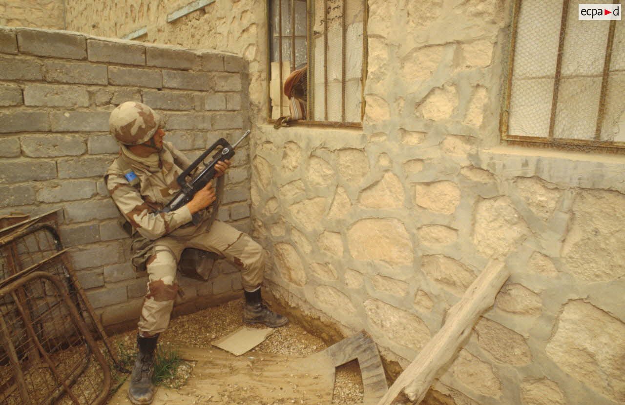 Un groupe de combat du 3e RIMa (r&eacute;giment d'infanterie de marine) fouille le village d'Al Salman. Un marsouin pointe son fusil d'assaut FAMAS dans la direction d'une fen&ecirc;tre d'o&ugrave; un habitant sort la t&ecirc;te.