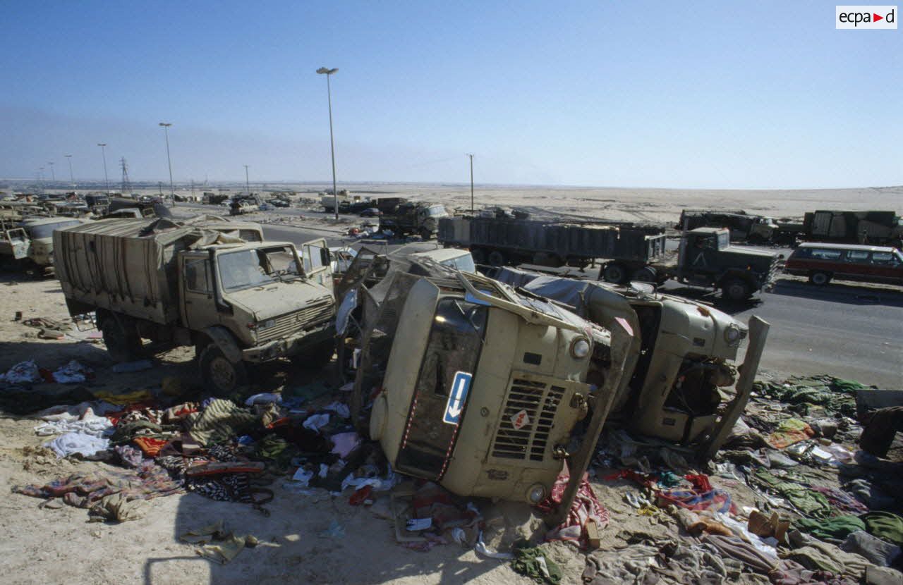 Carcasses de v&eacute;hicules d&eacute;truits et abandonn&eacute;s &agrave; la sortie de Koweit City, dont des camions Gaz-66 4x4. Des tissus jonchent le sol.