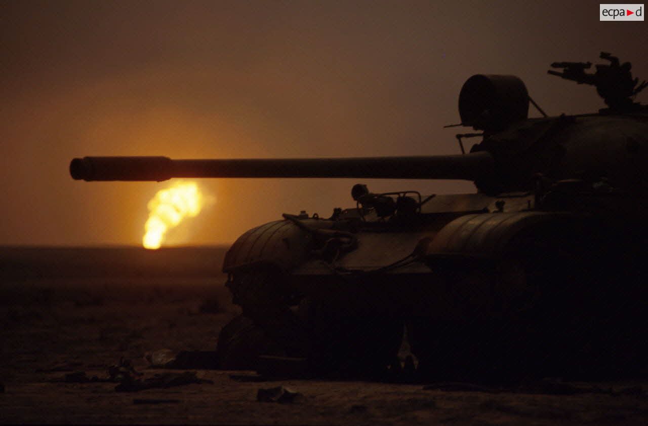Les puits de pétrole en feu aux environs de Koweit city derrière un char irakien T-55 détruit.