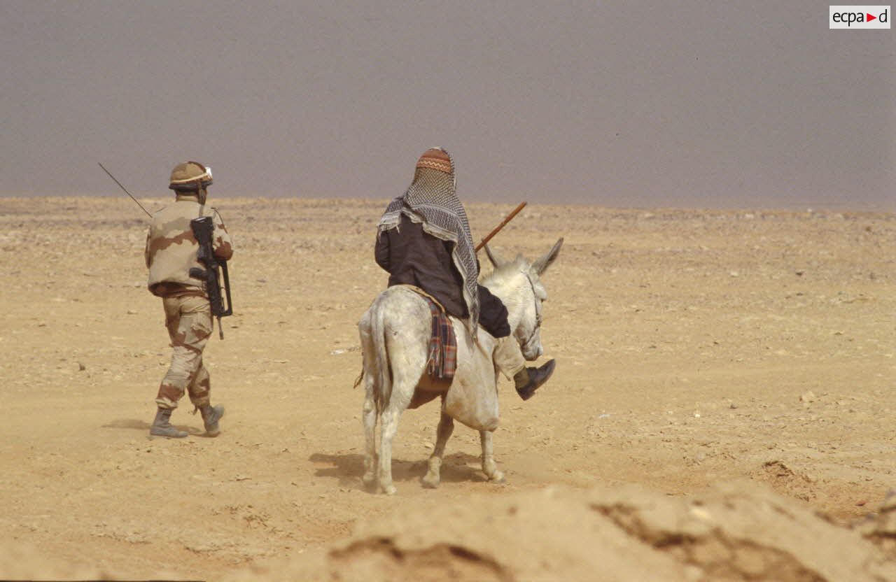 Une sentinelle française accompagne Un bédouin qui chevauche un âne aux abords du PC (poste de commandement) divisionnaire.