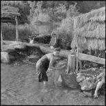 Une femme fait la toilette à son enfant dans la rivière.
