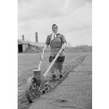 Dans une ferme réquisitionnée par l'armée allemande, une femme utilise une charrue pour retourner la terre.