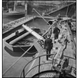 Chargement, à l'aide d'un palan, de torpilles dans les tubes lance-torpilles d'une tourelle orientable d'un sous-marin, à quai dans un port.