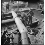 Chargement, à l'aide d'un palan, de torpilles dans les tubes lance-torpilles d'une tourelle orientable d'un sous-marin, à quai dans un port.