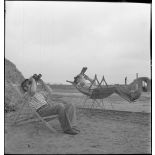 Des marins, appartenant à la 4e batterie de 90 mm contre avions, batterie mobile de défense antiaérienne de la Marine, observent le ciel à l'aide de jumelles, installés dans des chaises longues ou des sièges suspendus.