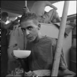 Portrait d'un prisonnier libéré par le Vietminh en train de boire dans un bol à bord d'un chaland de débarquement le rapatriant vers Haïphong.