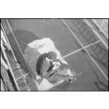 Vue en plongée sur l'aumônier du contre-torpilleur Le Malin, assis sur un des ponts du navire.