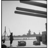 Sentinelle en faction sous une des tourelles du cuirassé Dunkerque. A  l'arrière-plan, le cuirassé Strasbourg amarré.