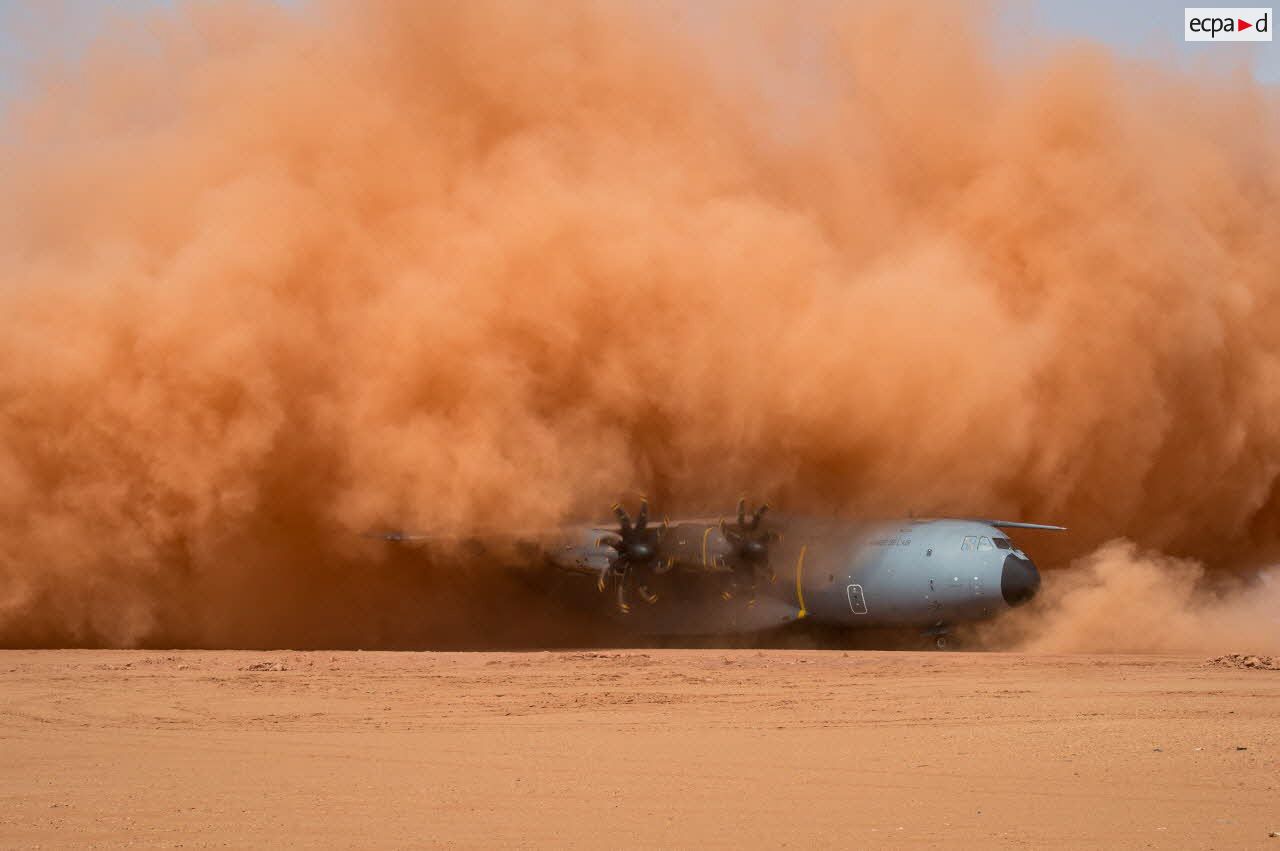 Atterrissage d'expérimentation d'un avion A400M sur la piste de Madama, dans un nuage de poussière ocre.