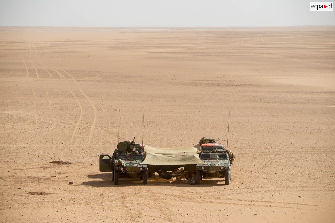 Des soldats d’une patrouille franco-nigérienne se reposent sur des hamacs tendus entre deux véhicules blindés légers (VBL) dans le désert nigérien.