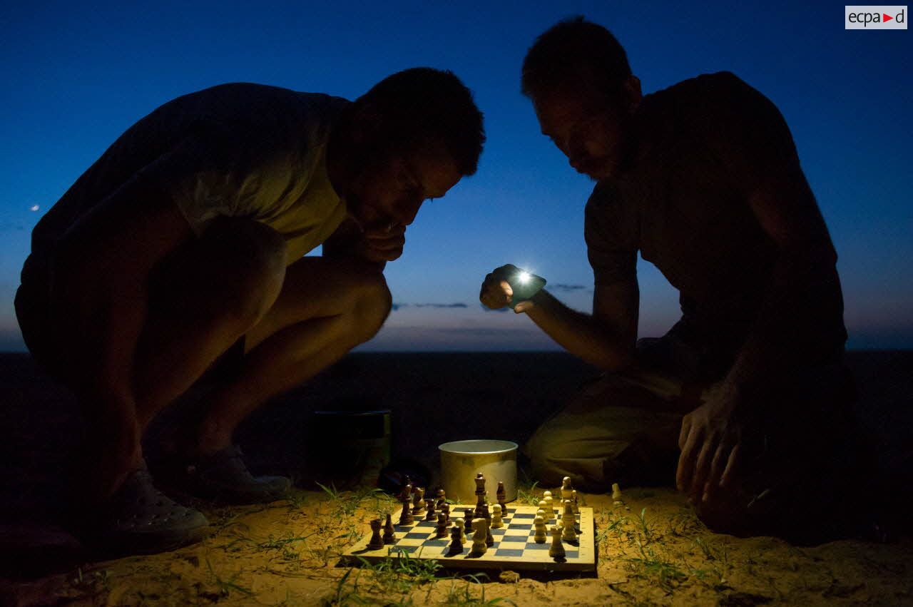 Des éléments du détachement de liaison et d'appui opérationnel n°3 (DLAO 3) disputent une partie d'échecs nocturne dans le désert malien.