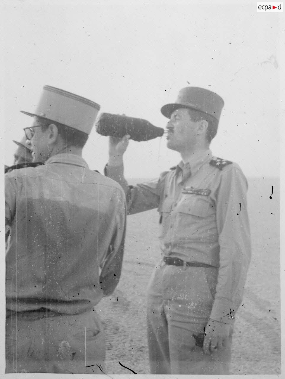 Photographie de profil du général Philippe Leclerc qui se désaltère, dans une région désertique.