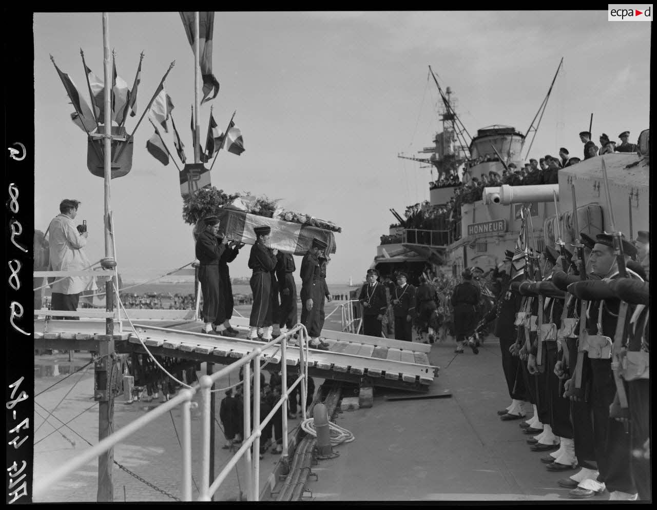 Des soldats transportent les cercueils du général Philippe Leclerc et de ses compagnons, à bord d'un croiseur, à quai, sur le port d'Alger.