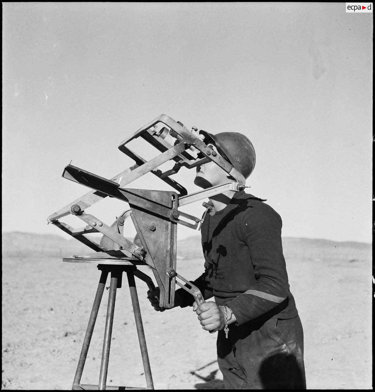 Un canonnier marin d'une batterie mobile de 90 de marine scrute le ciel avec des jumelles d'artillerie sur trépied.