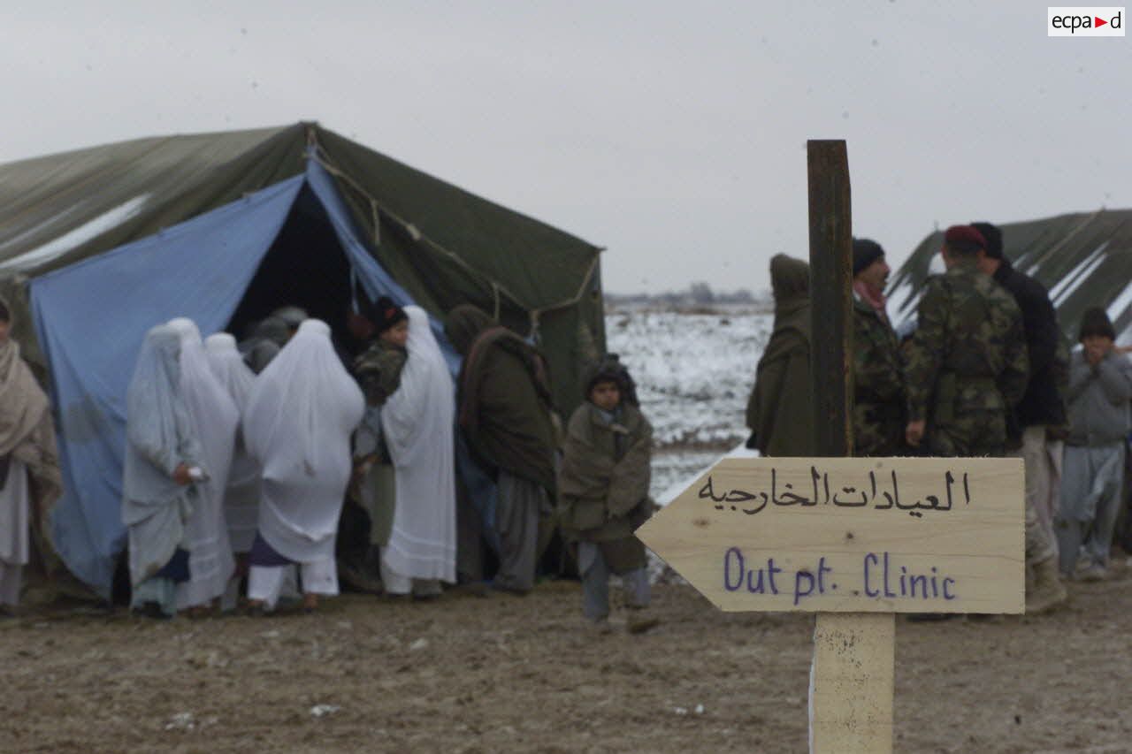 Consultations pour la population civile à l'hôpital jordanien de l'aéroport de Mazar e Charif. Affluence et file d'attente des femmes afghanes voilées venues consulter à l'entré de la tente d'admission. Un écriteau porte une inscription en arabe et en anglais "Out pt. clinic".