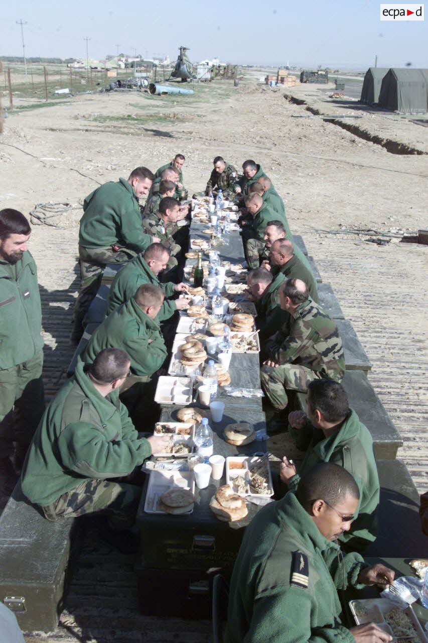 Dernier déjeuner en plein air des derniers militaires du détachement français présents à l'aéroport de Mazar e Charif avec des plateaux repas et sur des caisses de matériel constituant des sièges de fortune. Tablée des convives en présence du responsable de l'ordinaire.