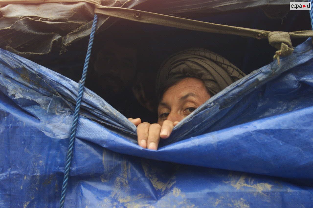 Camp de réfugiés afghans à Mazar e Charif. Les abris du camp sont fabriqués avec des matériaux de récupération pour lutter contre le froid et la pluie. Deux hommes s'abritent derrière des bâches.