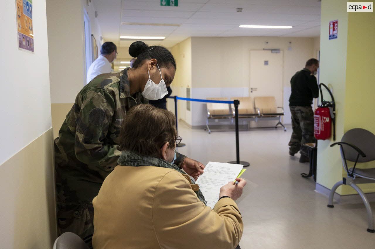 Un militaire aide une patiente à remplir son formulaire de vaccination au sein de l'hôpital d'instruction des armées (HIA) Bégin.