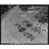 Plan en plongée d'un défilé de canons antiaériens, sous le regard de la population civile, à Alger.