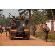 Des militaires français et italiens de l'EUFOR-RCA patrouillent à pied à proximité d'un blindé IVECO VTLM Lince italien (véhicule tactique léger multi-rôles), servi en tourelle par un militaire armé d'une mitrailleuse Rheinmetall MG-3 7,62 mm.