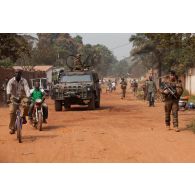 Des militaires français et italiens de l'EUFOR-RCA patrouillent à pied à proximité d'un blindé IVECO VTLM Lince italien (véhicule tactique léger multi-rôles), servi en tourelle par un militaire armé d'une mitrailleuse Rheinmetall MG-3 7,62 mm.