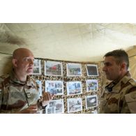 Visite du vice-amiral d'escadre Olivier Coupry, inspecteur général des armées, au camp Leclerc de la base aérienne Al-Asad Air Base (AAAB). Celui-ci s'entretient devant des photographies prises lors d'actions du 3e RAMa intégré à la Task Force Wagram avec le colonel Pierrick Michel, chef de corps du régiment.