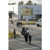 Des ressortissants évacués se dirigent vers leur avion pour l'embarquement sur l'aéroport de Tripoli (Libye), passant près d'une affiche représentant le colonel Kadhafi.