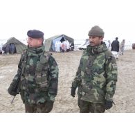 Consultations pour la population civile à l'hôpital jordanien de l'aéroport de Mazar e Charif. Le lieutenant-colonel Bordachar, commandant le détachement français, en compagnie d'un militaire jordanien devant les tentes d'admission où se pressent des femmes afghanes voilées venues consulter.