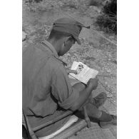 Un capitaine (Hauptmann), commandant la 5e batterie du Panzer Artillerie Regiment (Pz.Art.Rgt-155), assis devant sa tente, lit son courrier et Die Oase (l'oasis).