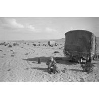 Un soldat fait la cuisine près d'un camion, au loin un canon de 5 cm PaK 38.