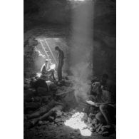 Deux soldats utilisent un téléphone de campagne dans la grotte sous un rayon de lumière. L'un d'eux fume.