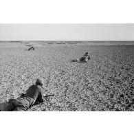 Un groupe de soldats allongés sur le sol observe le terrain. Tir de fusées dans le lointain.