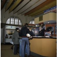 Une femme et un homme accueillent des étudiants sur le stand de l'exposition Jeunesse 1976, dans l'ancienne gare de la Bastille à Paris.