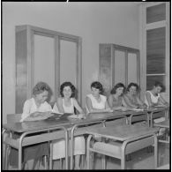 Jeunes femmes destinées à devenir monitrices assises à des bureaux dans une salle de classe.