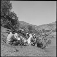 Des hommes du poste de Bou Maad en conversation avec des femmes et des éducatrices des équipes médico-sociales itinérantes (EMSI) au bord de l'oued.