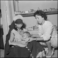 Portrait d'une femme et de son enfant assis, assistés par une monitrice, à l'intérieur d'une antenne médicale.