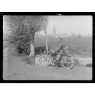 Roesbrugge. Vaguemestre sur motocyclette. Au fond l'église de Roesbrugge. [légende d'origine]