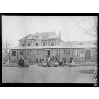 [Photographie de groupe rassemblant des enfants devant une école, accolée à une mairie, devant un bâtiment en reconstruction.]