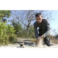 Un stagiaire confectionne une torche fumigène et  se nettoie les mains avec du sable lors d'un stage CSAR.