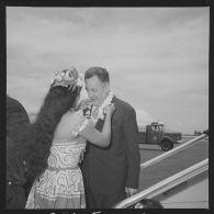 Le capitaine de vaisseau Bernoud, commandant du site de Moruroa (Mururoa), arrivant à Faa'a, l'aéroport de Papeete, se voit offrir un collier de fleurs par une hôtesse polynésienne en tenue traditionnelle.