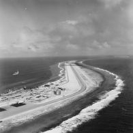 Vue aérienne de la piste d'atterrissage de Moruroa, de la zone portuaire, de la rade et de la force Alfa au mouillage ou à quai.