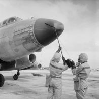 Au pied d'un avion Vautour, deux membres de l'équipe de décontamination en tenue de protection mesurent à l'aide d'un détecteur la radioactivité sur le nez de l'aéronef, sur l'atoll d'Hao.