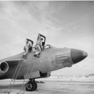 Juchés sur les échelles, deux mécaniciens en tenue de protection assistent les pilotes d'un avion Vautour installés aux cockpits, sur l'atoll d'Hao.