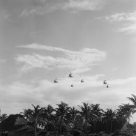 Vol en formation de six hélicoptères Alouette II, probablement du groupe aérien mixte 82 (GAM 82), en basse altitude au-dessus de la zone de vie à Moruroa.