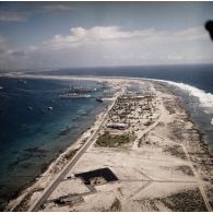 Vue aérienne des installations de l'atoll de Moruroa. Les bâtiments bases (BB) Médoc (A612) et Maurienne (A637) et le navire-atelier de mécanique et charpentage Garonne (A617) à quai. En arrière-plan, la piste d'atterrissage.